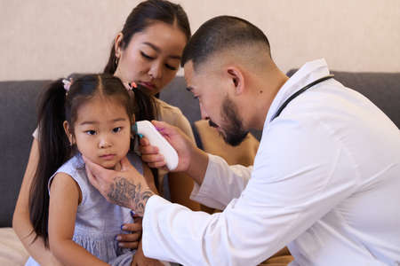 Caring otolaryngologist doctor looking through otoscope at Asian girl earsの写真素材