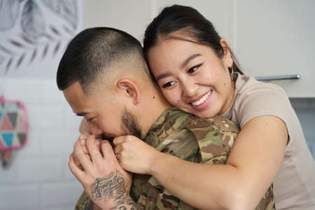 Beautiful smiling asian woman hugging her husband soldier in military clothesの写真素材