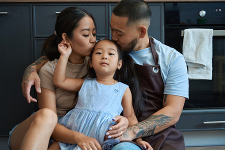 Mom and dad hug and kiss their little daughter on forehead