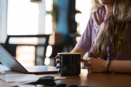 Woman sitting with a cup of coffee at her deskの写真素材