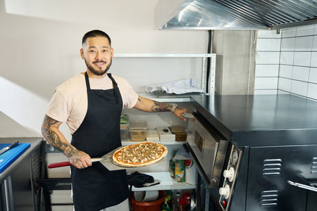 Friendly guy posing with a handmade pizza in kitchen