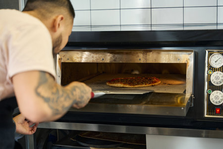 Hard-working man cooking delicious pizza in the ovenの写真素材