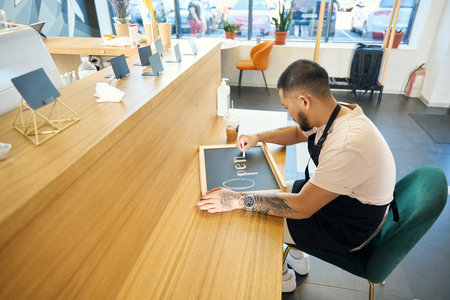 Enthusiastic young man preparing a chalkboard sign in his cafe