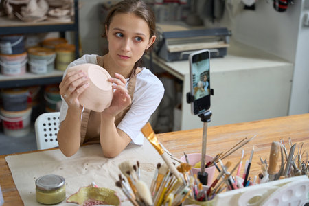Craftswoman sculpts a clay plate in front of phone camera