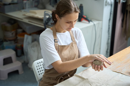 Woman sits at table and works with lump of clayの写真素材