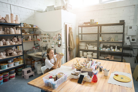 Pretty woman from light studio painting a clay plate