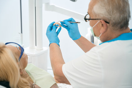 Unrecognized male doctor is pointing on artificial teeth in dental clinicの写真素材