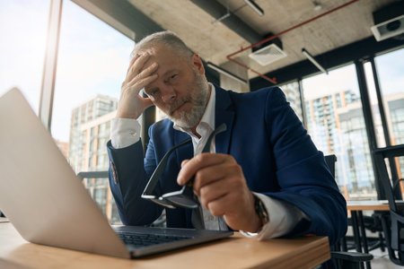 Serious mature businessman with laptop in officeの写真素材