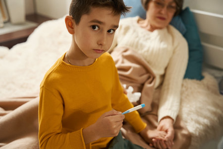 Young boy checking body temperature of elderly womanの写真素材