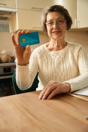 Elderly female showing card to camera at homeの写真素材
