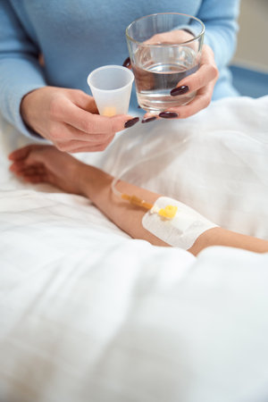 Adult woman gives pills and glass of water to sick childの写真素材