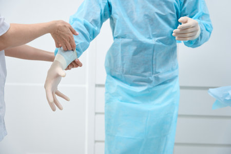 Close up of doctor in light-blue disposable medical suit putting gloves onの写真素材