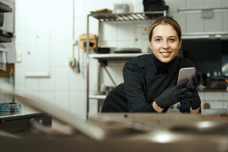 Smiling chef stands in restaurant kitchen with phone in her hands