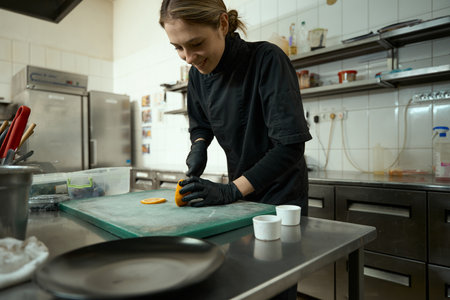Young woman cuts orange for fruit salad, kitchen equipment around