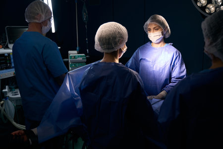 Group of people in surgical overalls stand at operating tableの写真素材
