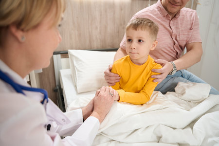 Neat child on the medical bed is looking to the doctor in the wardの写真素材
