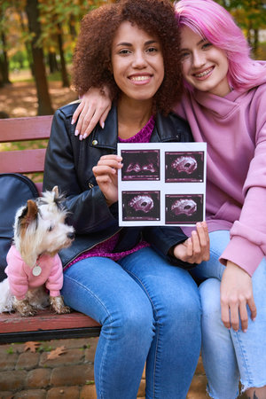 Happy lesbian couple showing ultrasound photos of their unborn babyの写真素材