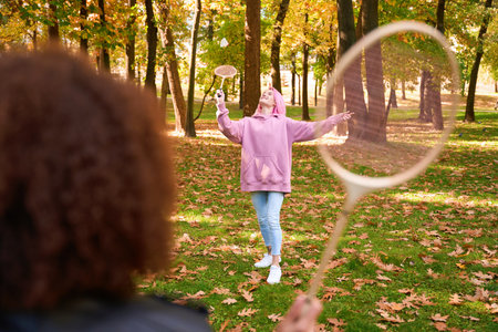 Joyful woman playing badminton with friend on lawn in parkの写真素材