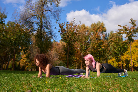 Joyous interracial sportwomen performing isometric core exercise outdoorsの写真素材