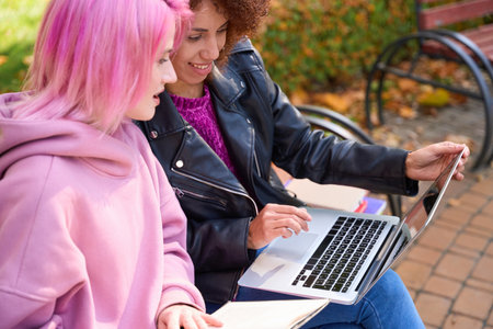 Women seated on bench watching something on laptop screenの写真素材
