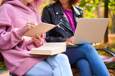 Woman taking notes in notebook beside friend using laptopの写真素材