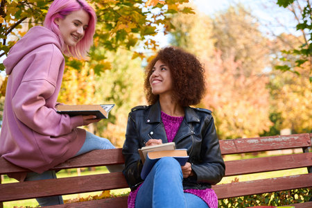 Joyous female students doing homework in parkの写真素材