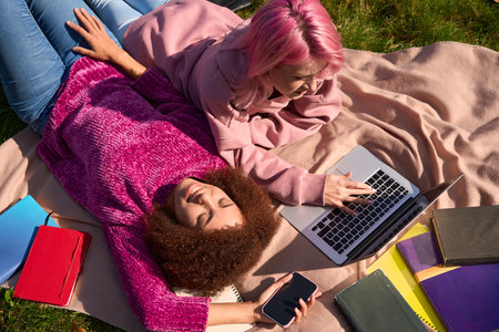 Cheerful lady resting while her friend working on portable computerの写真素材