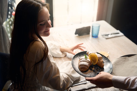 Beautiful young woman is treated to a croissant by companionの写真素材