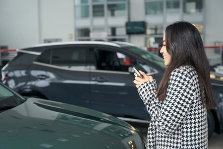 Asian female stands in a car dealership with car keysの写真素材