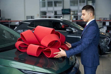Nice smiling man attaches red gift bow to hood carの写真素材
