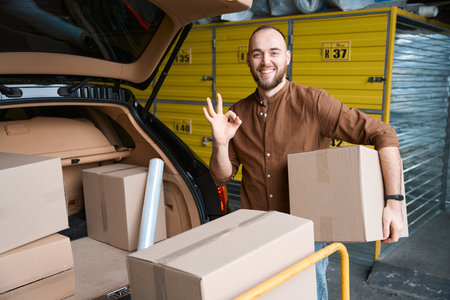 Happy young man holding a box and showing ok