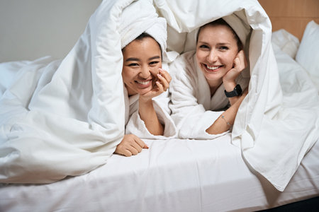 Cute women peek out from under covers on bedの写真素材