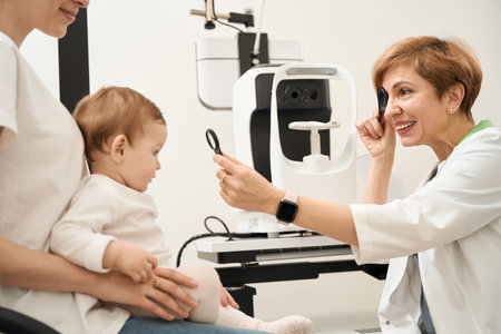 Cheerful oculist examining little child eyes in presence of parentの写真素材
