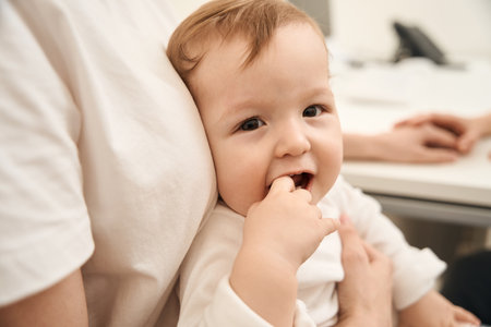 Baby touching bottom teeth with finger during pediatric doctor consultationの写真素材