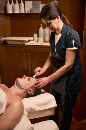Concentrated beautician performing facial skin rejuvenation treatment on clientの写真素材