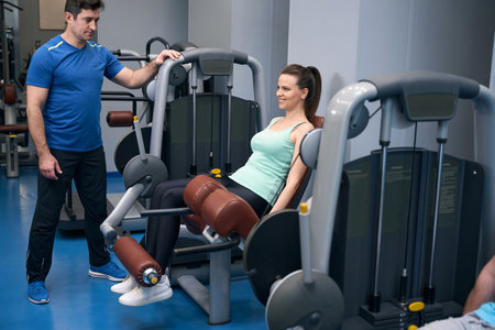 Joyous sporty woman doing lower-body workout supervised by personal trainer