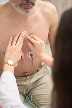 Doctor preparing man for electrocardiography in the clinic