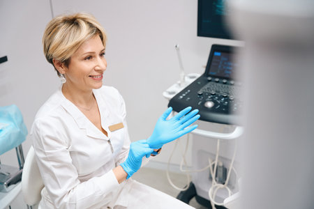 Joyful woman gynecologist wearing medical gloves before examining patientの写真素材