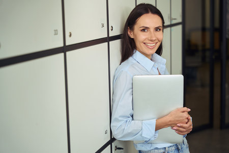 Cheerful office worker posing for camera with computer in handsの写真素材