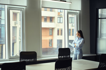 Pensive young company manager contemplating cityscape from empty officeの写真素材
