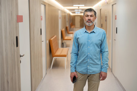 Adult man with phone standing in hallway of hospitalの写真素材