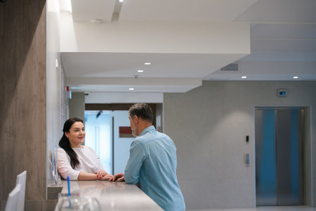 Beautiful female paramedic leaning on reception desk communicating with patientの写真素材