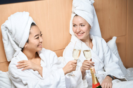 Girlfriends in white coats drinking champagne in a hotelの写真素材