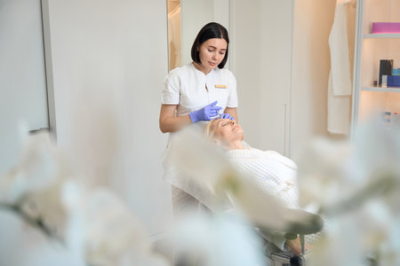 Beautician in gloves performing injection on client foreheadの写真素材
