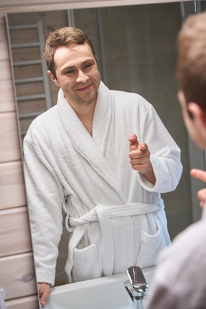 Happy male looks at himself in the bathroom mirrorの写真素材