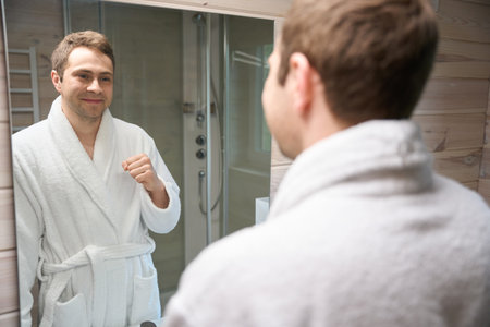 Male in bathrobe looking at himself in bathroom mirrorの写真素材