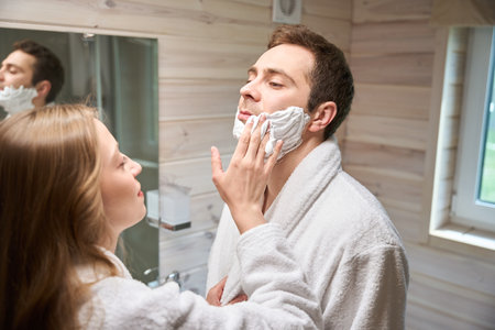 Woman applying shaving foam to man face in bathroomの写真素材