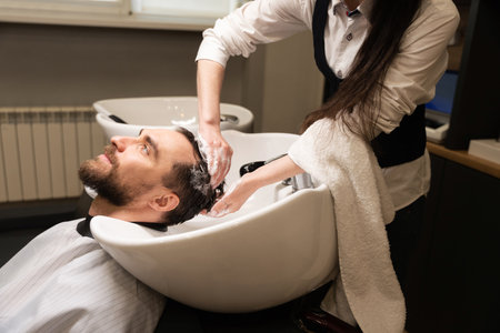 Handsome man enjoys procedure of washing his hair in barbershopの写真素材