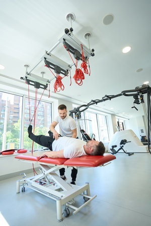 Man working out with suspended straps aided by gym coach