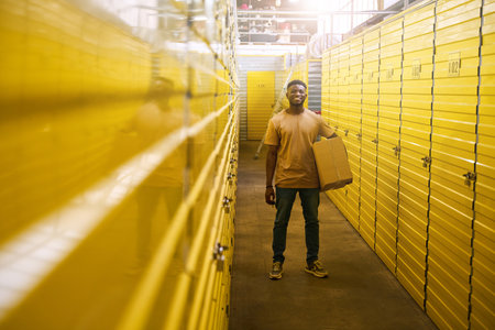 African American guy in jeans stands with cardboard box near containersの写真素材